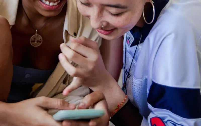 Zwei Frauen der Gen Z sehen sich Content auf einem Handy an und lachen über den Inhalt