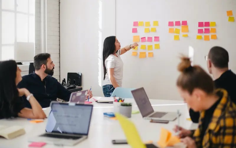 In a meeting, an editorial team discusses what content they will fill their next liveblog with using post it notes on a whiteboard. 