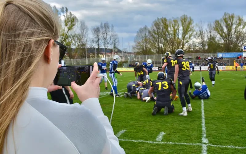 Mädchen nutzt Tickaroo Live Sports auf ihrem Handy, um ein American Football-Spiel vom Spielfeldrand aus zu filmen