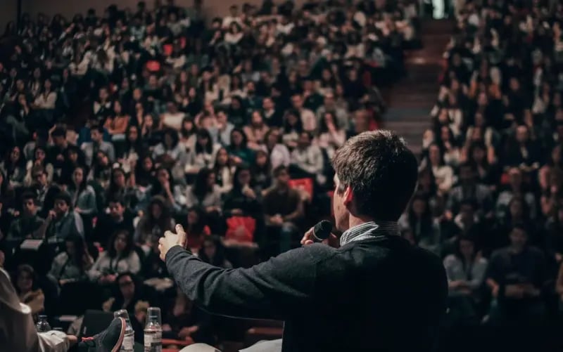 Eine große Halle mit vielen sitzenden Menschen. Vorne auf der Bühne steht ein Speaker, der über die neuesten technologischen Entwicklungen spricht. Die Convention wird mit einem Liveblog verfolgt und ermöglicht dadurch auch Menschen, die nicht live vor Ort dabei sein können, eine seriöse Berichterstattung des Events in Echtzeit. 