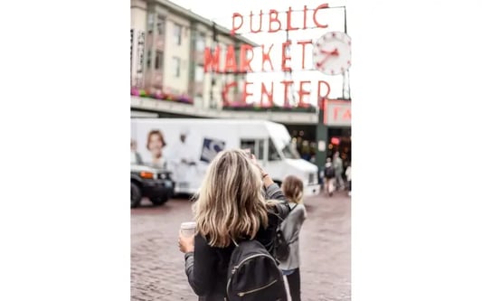 Woman photographs a red neon sign that reads "Public Market Center" with her smartphone. 