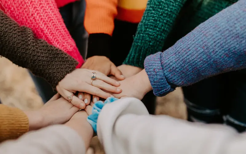8 Personen legen in der Mitte eines Kreises ihre Hände aufeinander, um Vertrauen zu symbolisieren. 