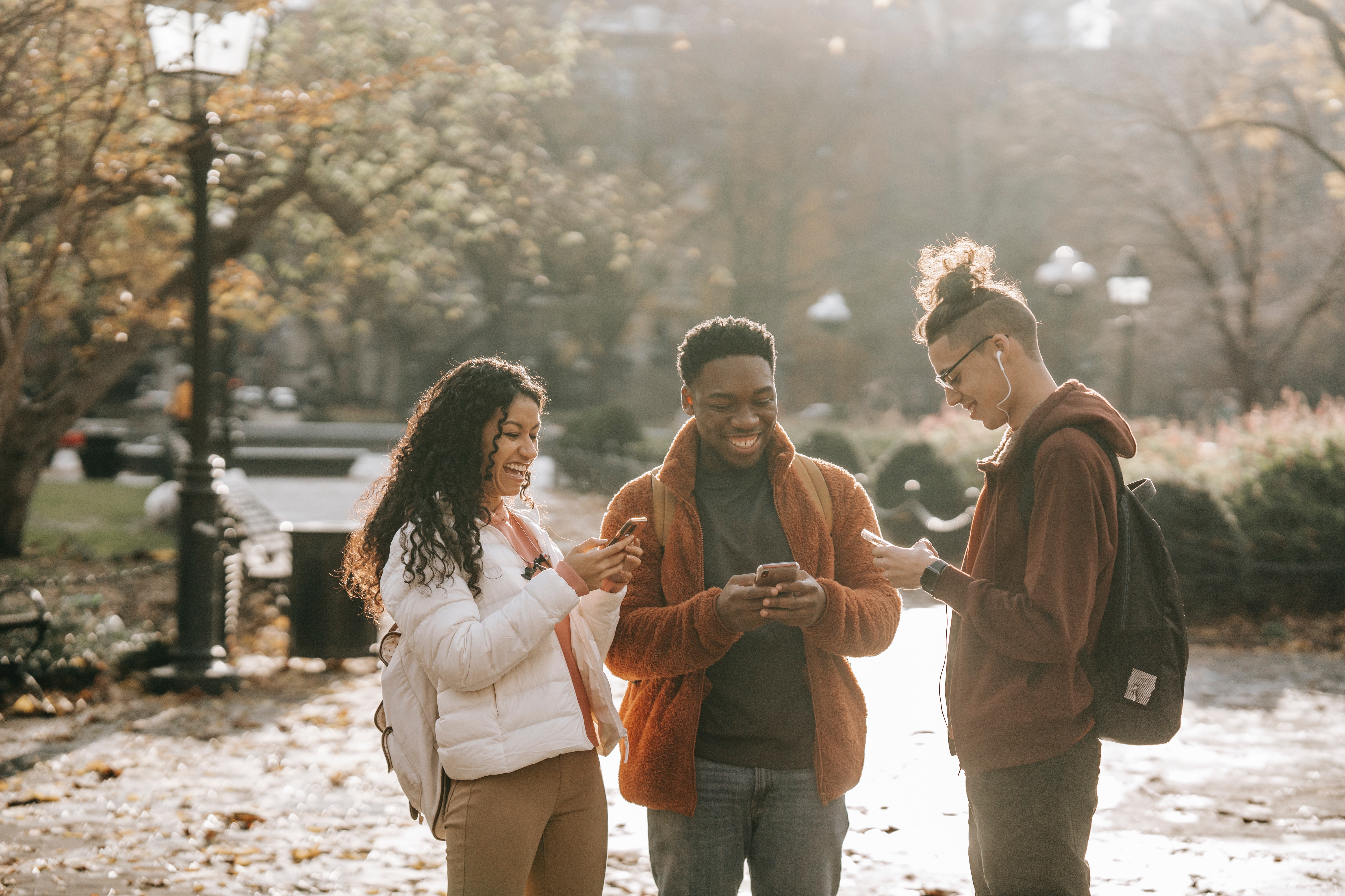 3 young people laughing while engaging with something on their phones and each other