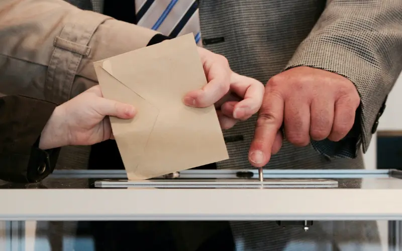 A person votes with a paper ballot, by placing it in a ballot box. 