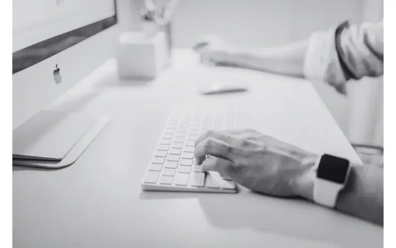 Person, die mit einer Apple-Tastatur tippt und an einem Computer arbeitet