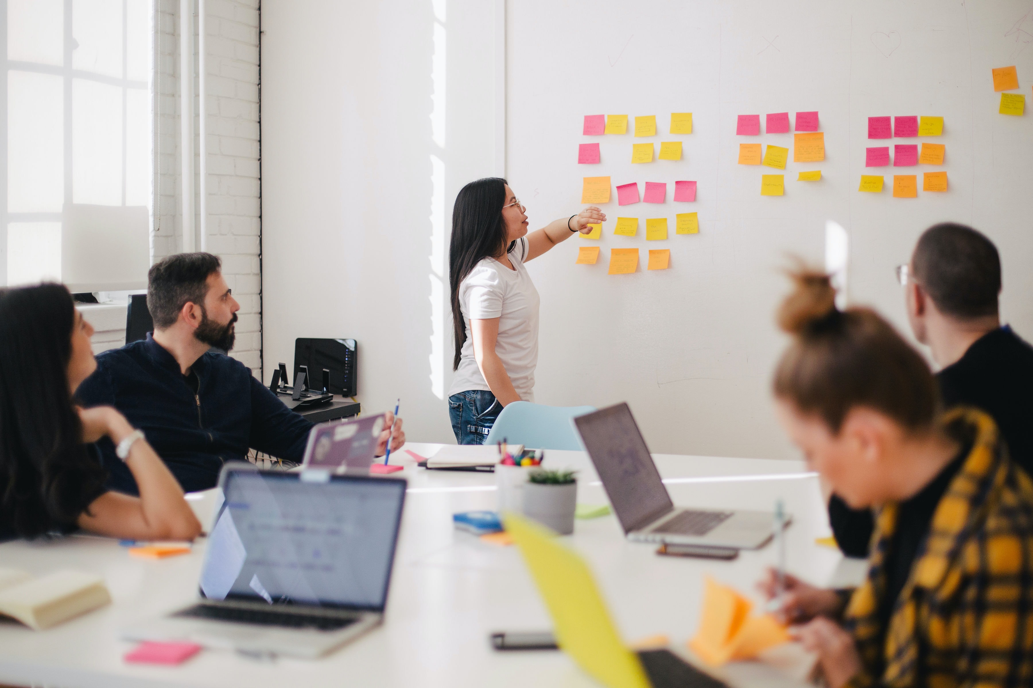 In a meeting, an editorial team discusses what content they will fill their next liveblog with using post it notes on a whiteboard.