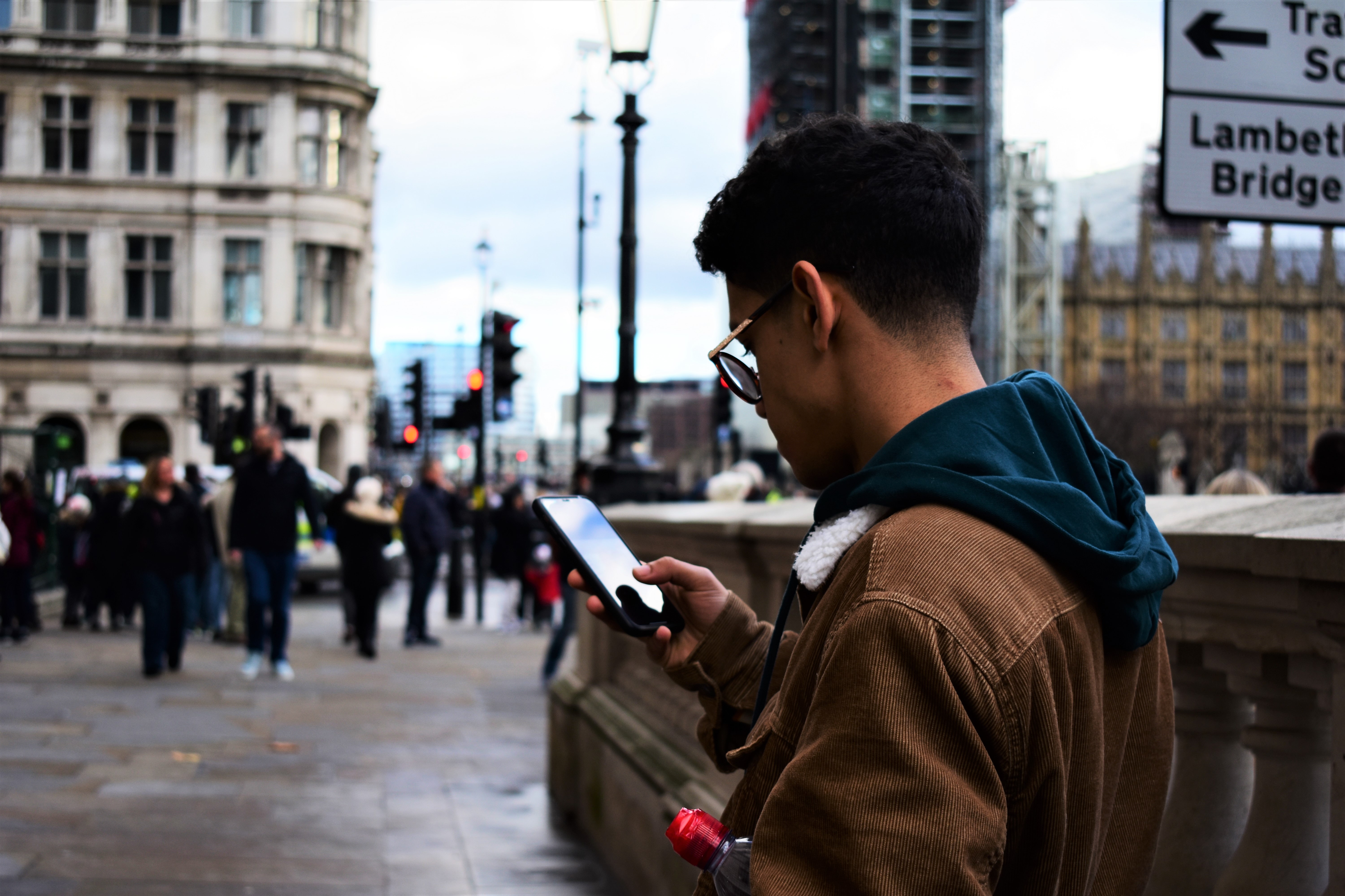 Ein junger Mann steht draußen in der Innenstadt an einer Brücke, hat sein Smartphone in der Hand und informiert im Kommunen Live Blog über die neuen kommunalen Verordnungen seiner Stadt.